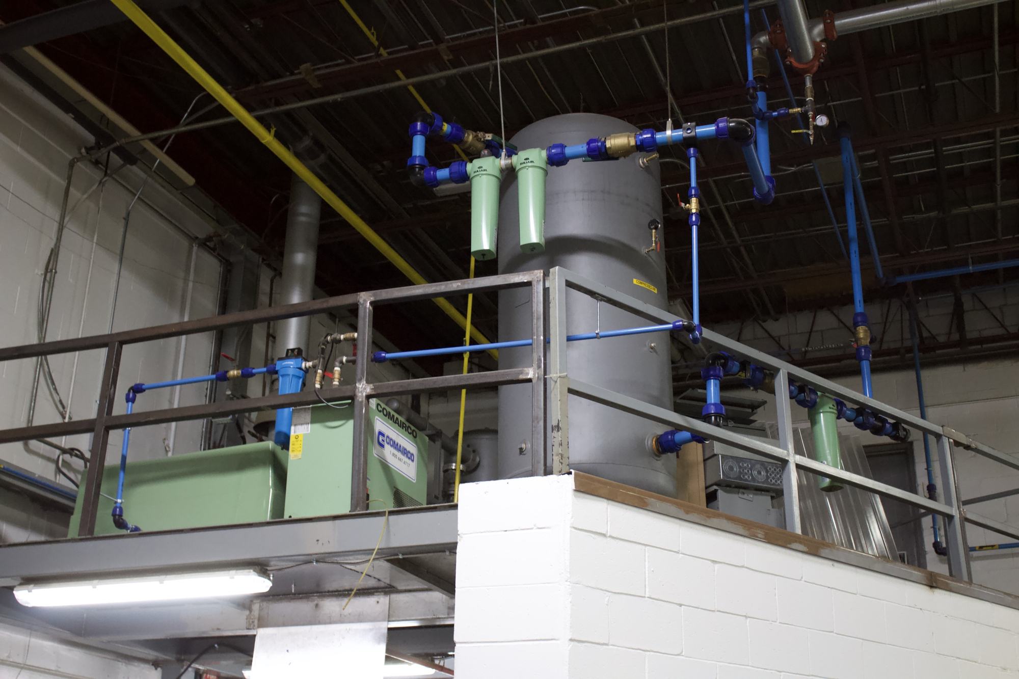 Compressed air receiver tank, filters and blue aluminum air piping on a mezzanine